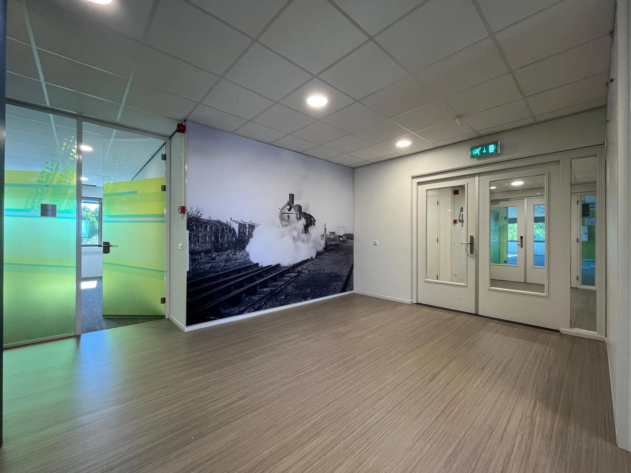 Hal met glazen deuren, houten vloer en een grote zwart-wit muurfoto van een stoomtrein aan de Barchman Wuytierslaan.